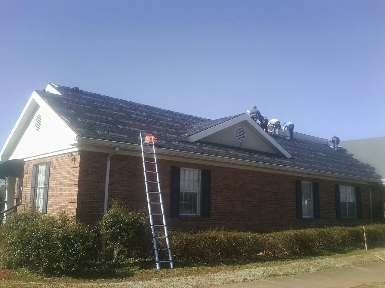 Crew tearing shingles off a brick ranch roof with a ladder set — Emergency Roof Repair work by our crew in Mont Vernon