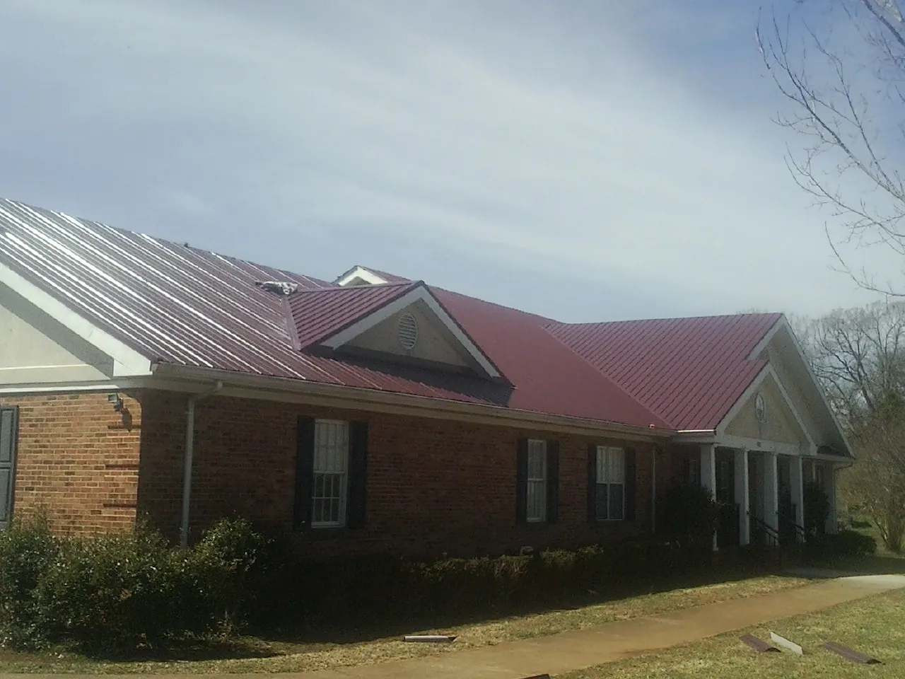 Red metal roof with gabled entries on a long brick building, from a Hail Damage Roof Repair job in Mont Vernon