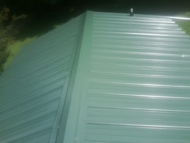 New green metal panels meeting at the ridge of a roof — Flat Roof Repair work by our crew in Mont Vernon