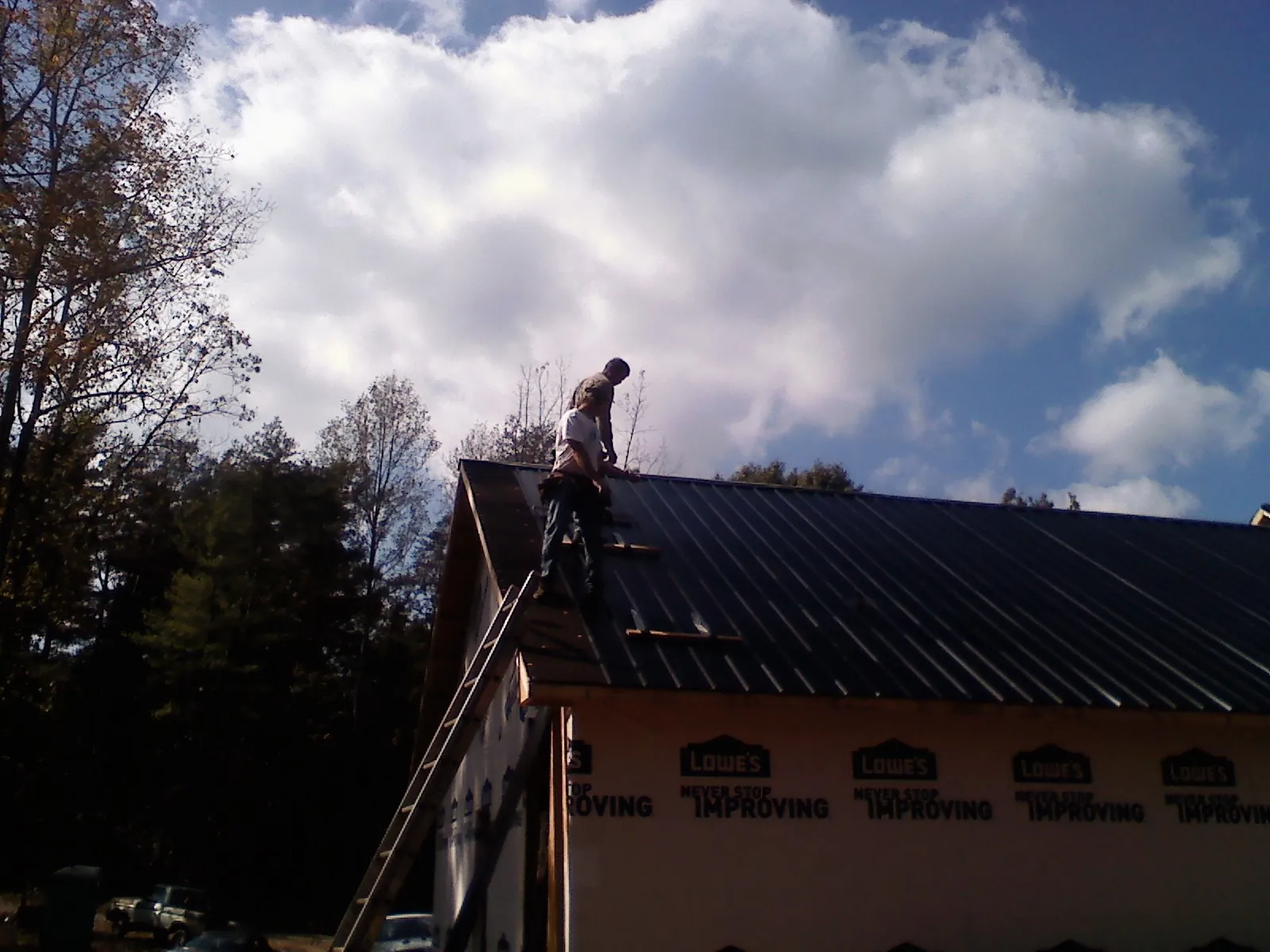 Roofer fastening dark metal panels high against a cloudy sky, from a Roof Inspection job in Mont Vernon