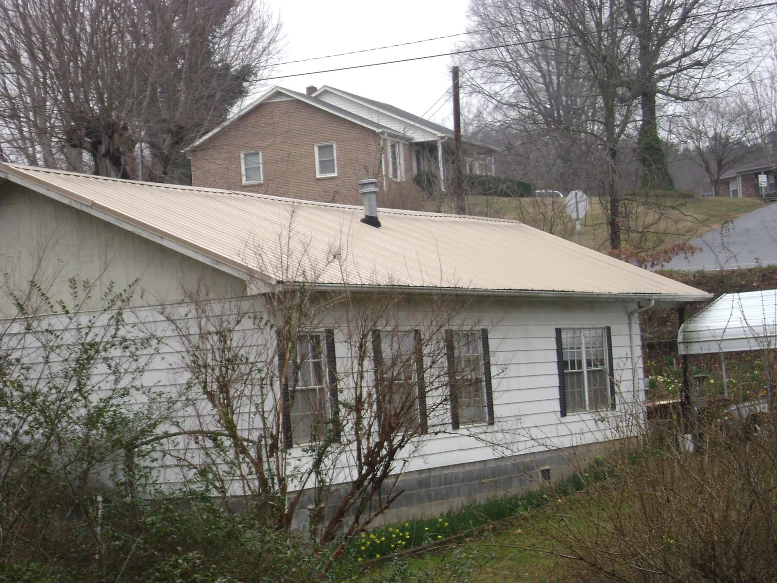 Tan metal roof on a white sided house set into a hillside — Commercial Roofing by Roofing Brothers in Mont Vernon